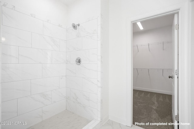 bathroom with a walk in closet, baseboards, and a tile shower