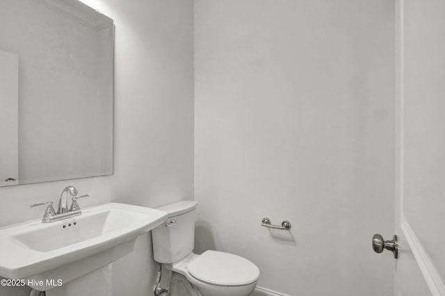 half bath featuring toilet, baseboards, and a sink
