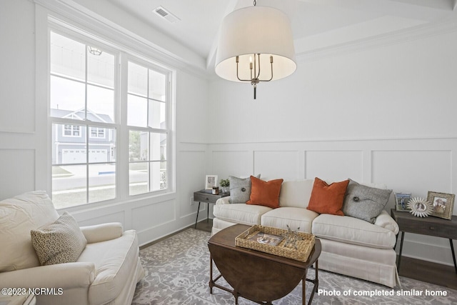 living area featuring crown molding, a decorative wall, an inviting chandelier, and wood finished floors