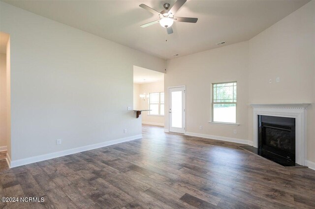 unfurnished living room with ceiling fan with notable chandelier, baseboards, a glass covered fireplace, and dark wood finished floors