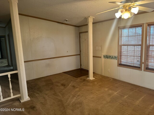 unfurnished room with a textured ceiling, dark carpet, ceiling fan, and decorative columns