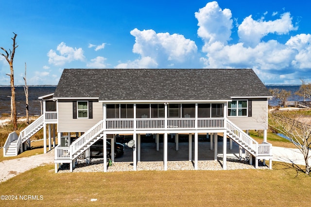 rear view of property featuring a sunroom, a water view, and a lawn