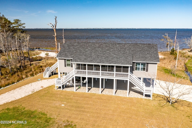 back of property featuring a sunroom, a water view, and a lawn