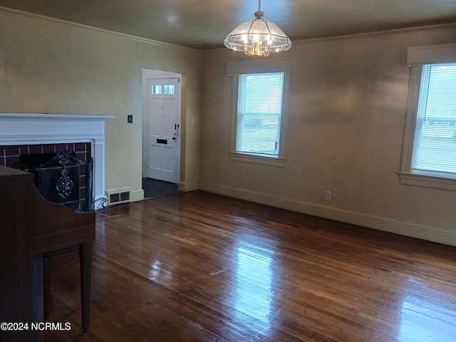 unfurnished living room featuring a healthy amount of sunlight, a tile fireplace, dark hardwood / wood-style floors, and an inviting chandelier