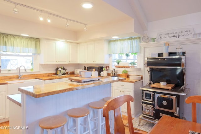 kitchen featuring a kitchen bar, track lighting, white cabinets, and a wealth of natural light