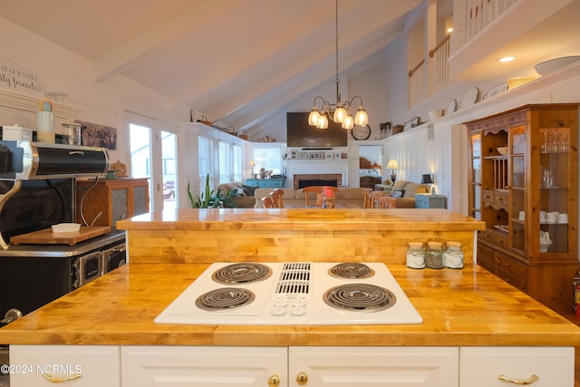 kitchen featuring an inviting chandelier, white cabinetry, butcher block countertops, white electric stovetop, and beam ceiling