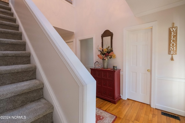 stairs with crown molding and light hardwood / wood-style floors