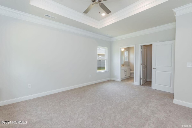 unfurnished bedroom with crown molding, ensuite bath, ceiling fan, a tray ceiling, and light carpet