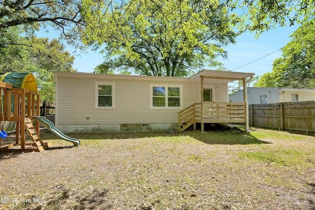 rear view of property with a playground and fence