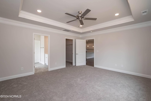 unfurnished bedroom with a closet, a walk in closet, a tray ceiling, and ceiling fan