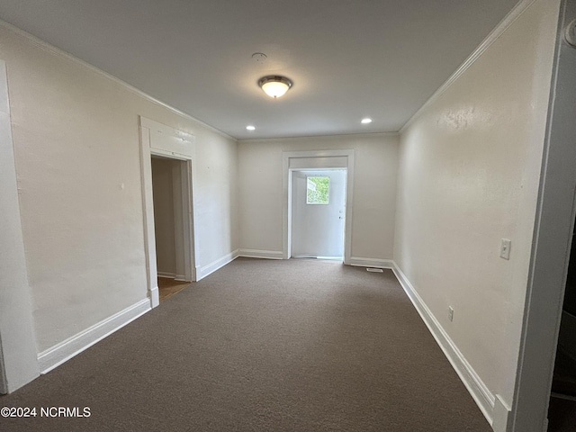 spare room featuring crown molding and dark colored carpet