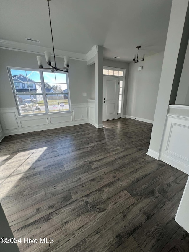 unfurnished living room with crown molding, dark hardwood / wood-style flooring, and an inviting chandelier