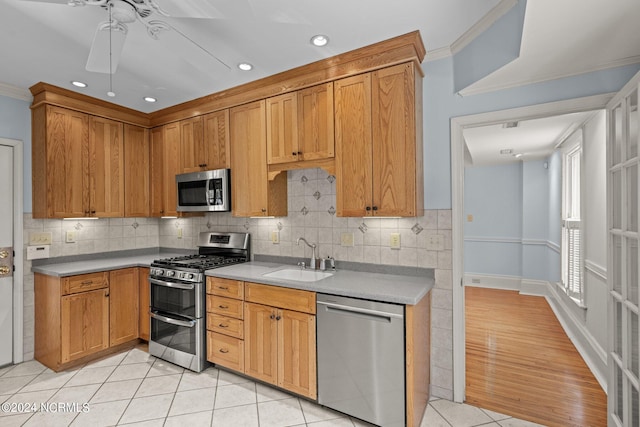 kitchen with appliances with stainless steel finishes, sink, light tile patterned floors, crown molding, and tasteful backsplash