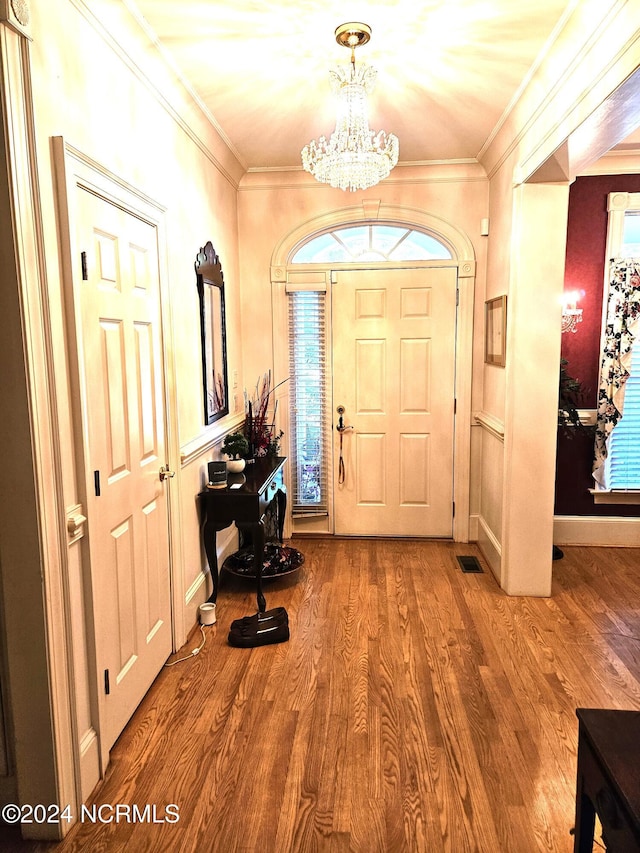 entrance foyer featuring wood-type flooring, ornamental molding, and a chandelier