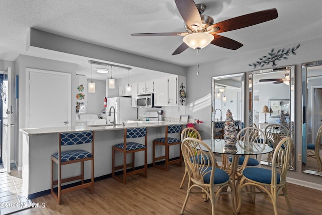 dining area with ceiling fan, a textured ceiling, sink, and light hardwood / wood-style floors