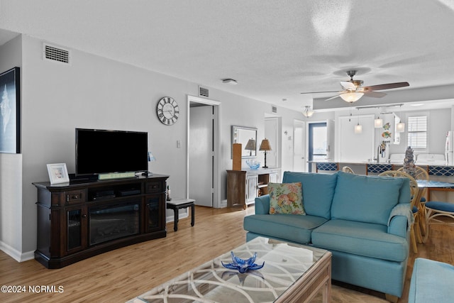 living room with a textured ceiling, light hardwood / wood-style floors, and ceiling fan