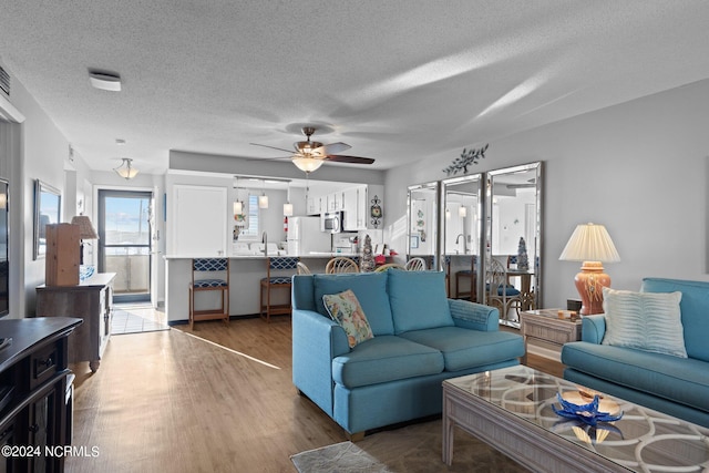 living room with ceiling fan, a textured ceiling, and dark wood-type flooring