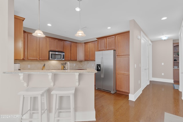 kitchen featuring decorative light fixtures, tasteful backsplash, light hardwood / wood-style flooring, and appliances with stainless steel finishes