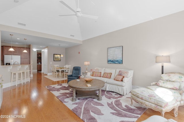 living room with light hardwood / wood-style flooring, ceiling fan with notable chandelier, and high vaulted ceiling