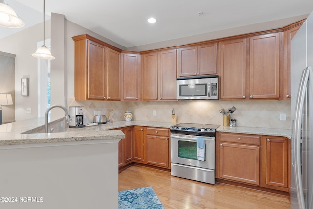 kitchen with appliances with stainless steel finishes, kitchen peninsula, light stone countertops, and light hardwood / wood-style flooring