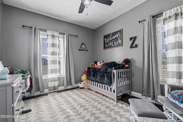 carpeted bedroom featuring a crib, multiple windows, and ceiling fan