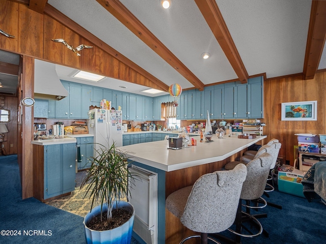 kitchen with blue cabinetry, dark colored carpet, white fridge, wooden walls, and a kitchen island