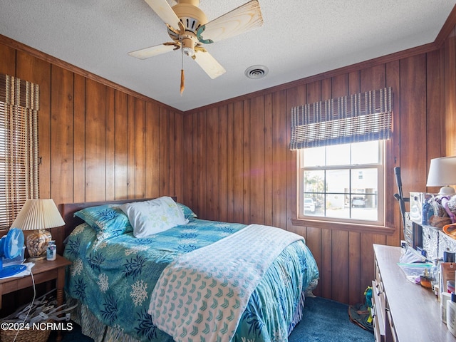 carpeted bedroom with ceiling fan, a textured ceiling, and wooden walls