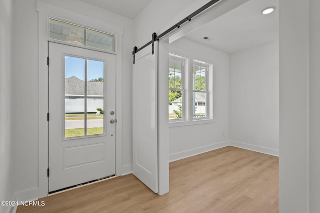 entryway with light wood-type flooring, a barn door, visible vents, and baseboards