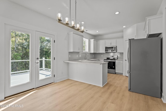 kitchen with a peninsula, light wood-type flooring, appliances with stainless steel finishes, and tasteful backsplash