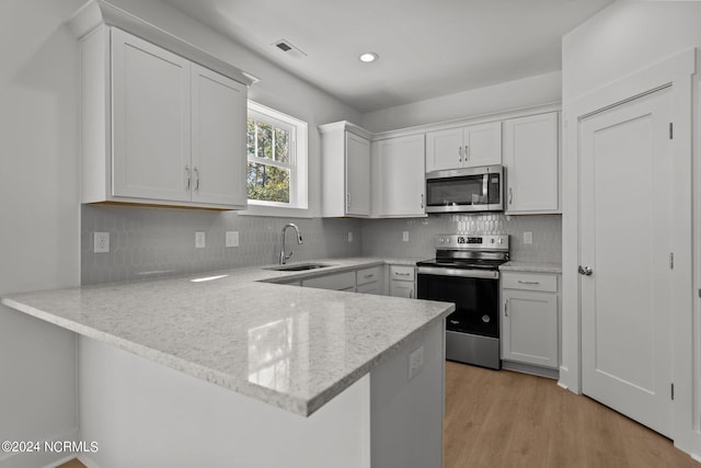 kitchen featuring decorative backsplash, appliances with stainless steel finishes, a peninsula, light wood-style floors, and a sink