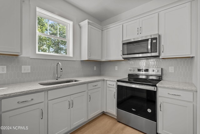 kitchen featuring light wood finished floors, backsplash, appliances with stainless steel finishes, white cabinets, and a sink