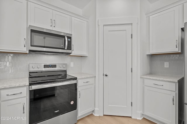 kitchen with white cabinets, appliances with stainless steel finishes, light wood-style flooring, and tasteful backsplash