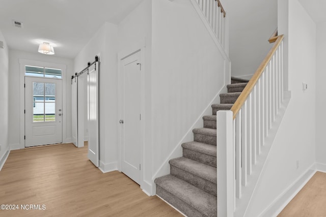 interior space with a barn door, visible vents, baseboards, stairs, and light wood-style floors