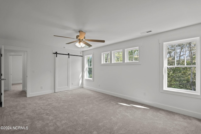 unfurnished bedroom with a barn door, carpet, visible vents, and baseboards