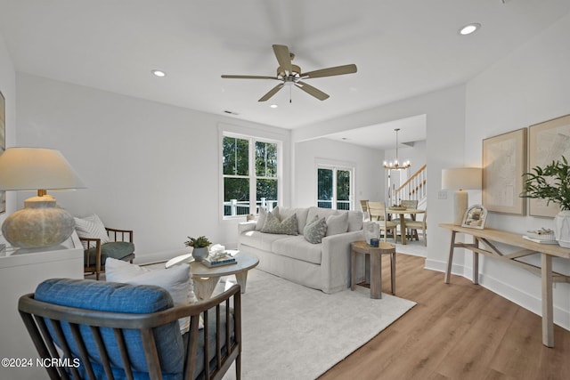 living room featuring recessed lighting, ceiling fan with notable chandelier, visible vents, baseboards, and light wood-style floors