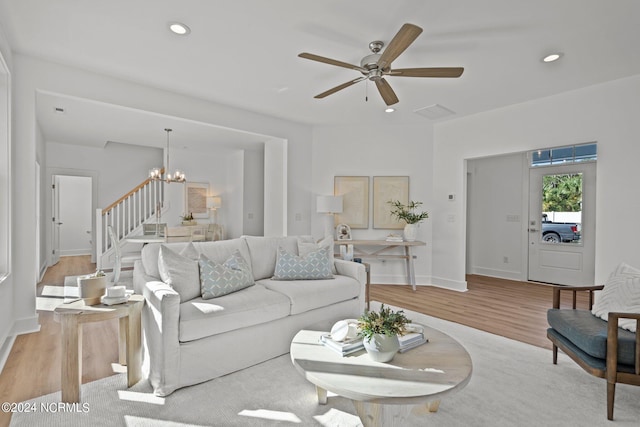 living room featuring recessed lighting, baseboards, stairway, light wood-style floors, and ceiling fan with notable chandelier