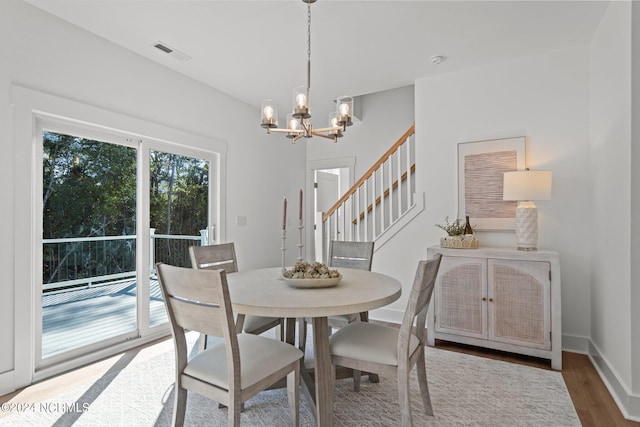 dining room with a notable chandelier, wood finished floors, visible vents, baseboards, and stairway