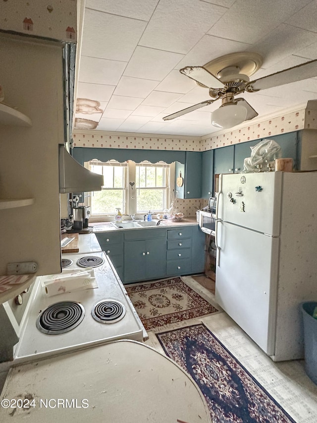 kitchen featuring white fridge, blue cabinetry, ceiling fan, wall chimney range hood, and light tile flooring