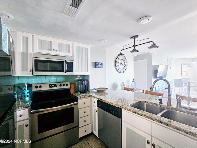 kitchen with stainless steel appliances, backsplash, hanging light fixtures, light stone counters, and sink