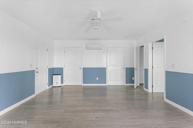 empty room featuring ceiling fan, a wall mounted AC, wood finished floors, and baseboards