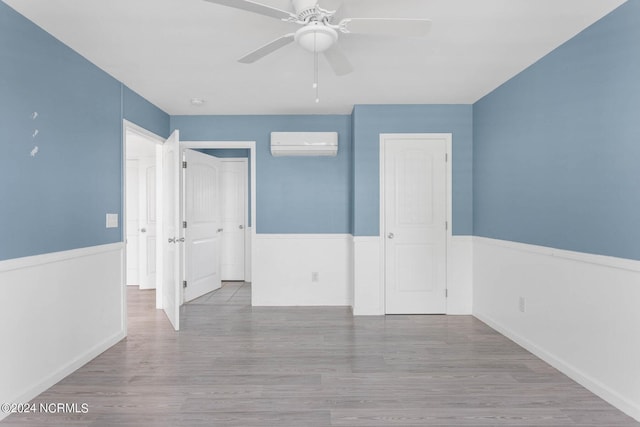 spare room featuring wood finished floors, wainscoting, ceiling fan, and a wall mounted AC