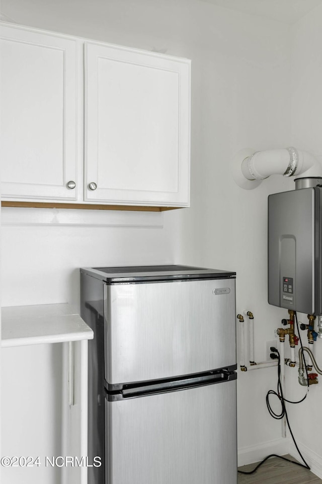 interior details with tankless water heater, freestanding refrigerator, and white cabinetry