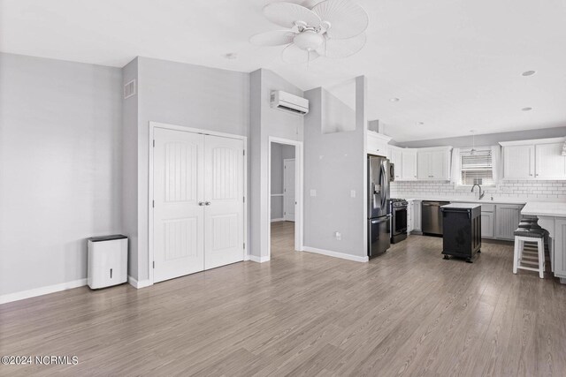 living room with vaulted ceiling, ceiling fan, sink, hardwood / wood-style flooring, and an AC wall unit