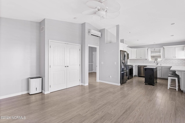 kitchen with light countertops, appliances with stainless steel finishes, light wood-type flooring, backsplash, and a wall mounted air conditioner