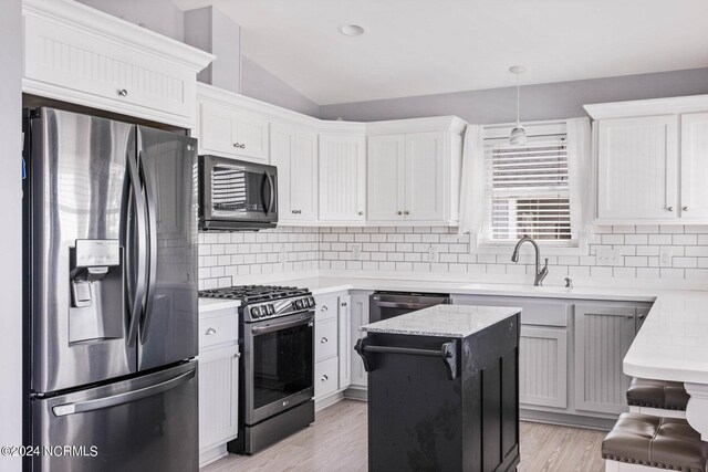 kitchen featuring lofted ceiling, white cabinets, decorative light fixtures, and appliances with stainless steel finishes