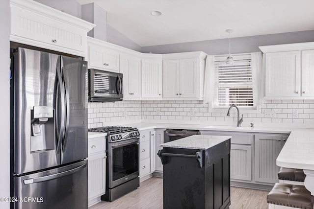 kitchen with lofted ceiling, appliances with stainless steel finishes, backsplash, and light wood-style floors