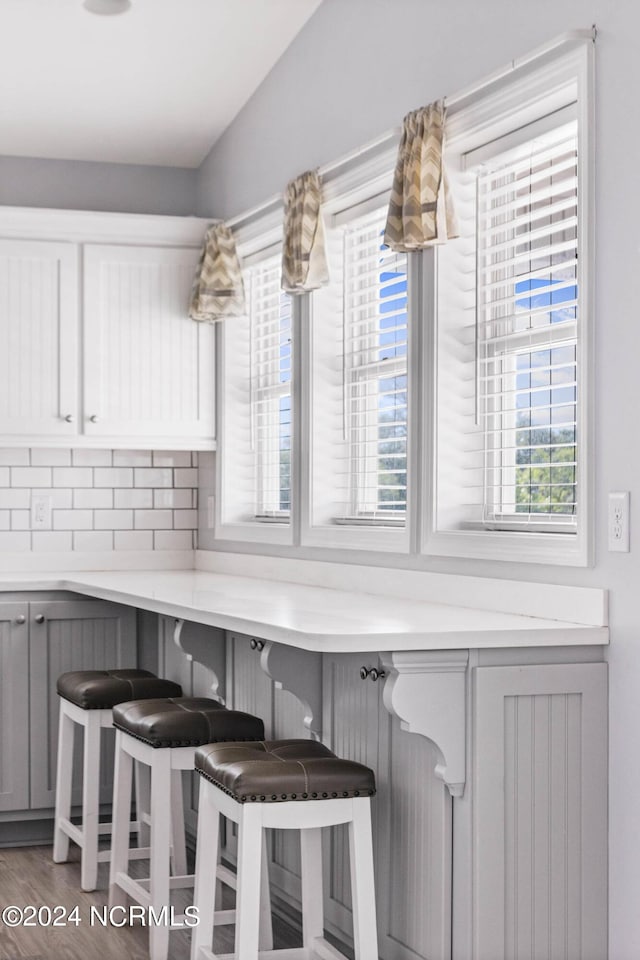 kitchen featuring dark wood-type flooring, gray cabinets, a kitchen breakfast bar, and backsplash