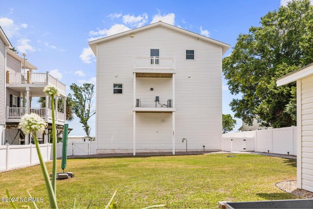 rear view of house featuring a fenced backyard, a balcony, a gate, and a yard