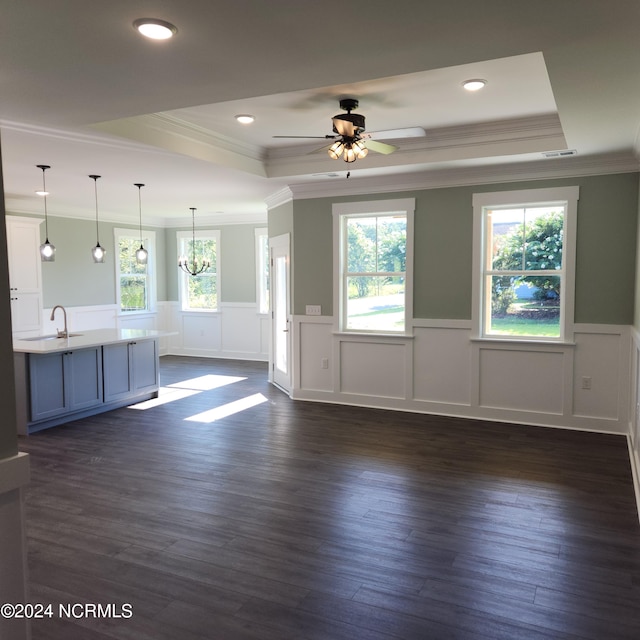 unfurnished living room featuring a tray ceiling, ceiling fan with notable chandelier, dark hardwood / wood-style floors, and ornamental molding