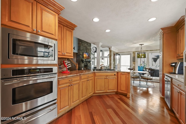 kitchen with light stone countertops, light hardwood / wood-style flooring, kitchen peninsula, and appliances with stainless steel finishes